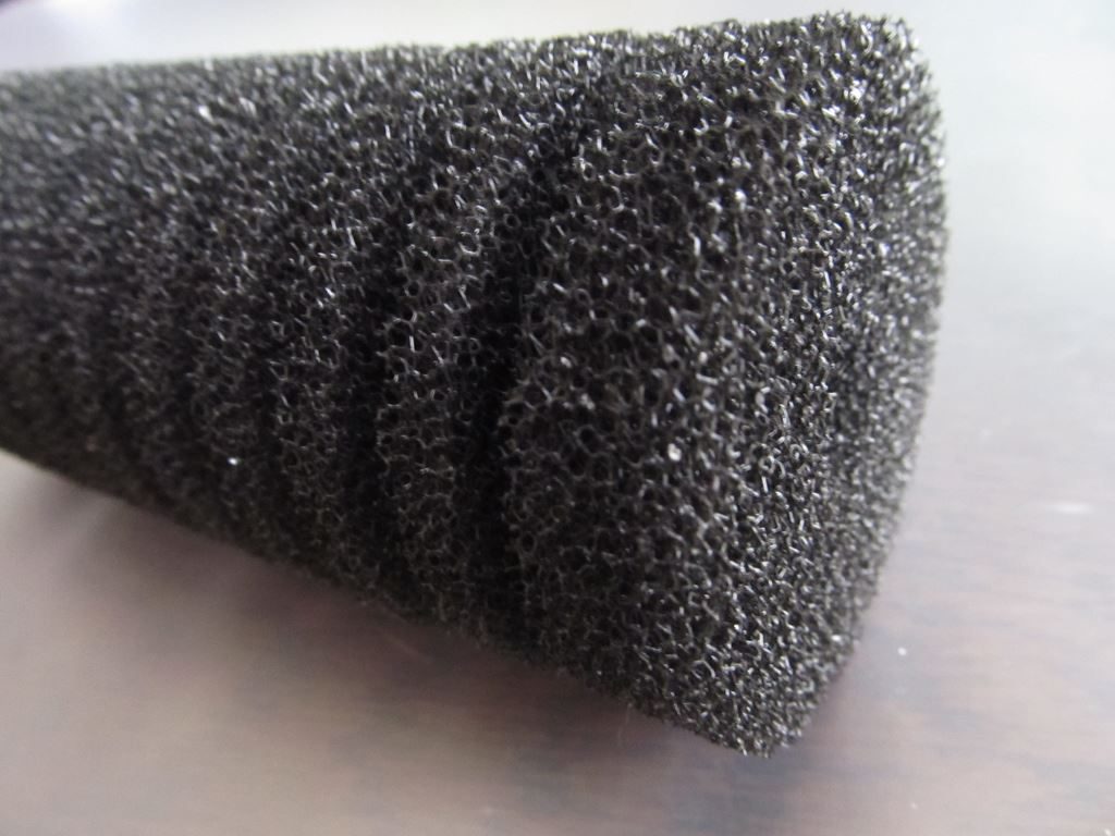 A cone of coarse black aquarium filter foam standing on a pale surface, its open-cell structure clearly visible.